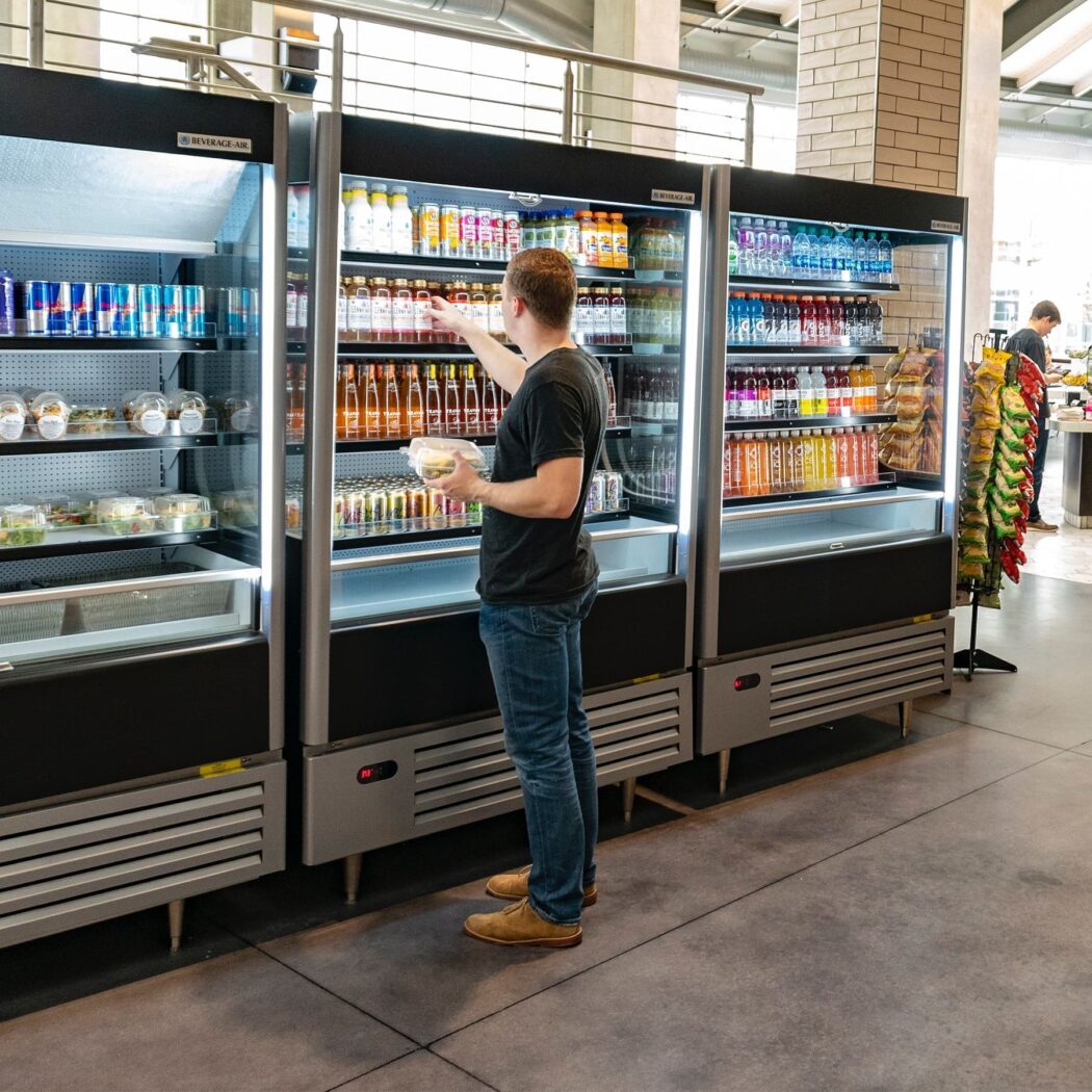 customer shopping for beverages from a set of open beverage air fridges.