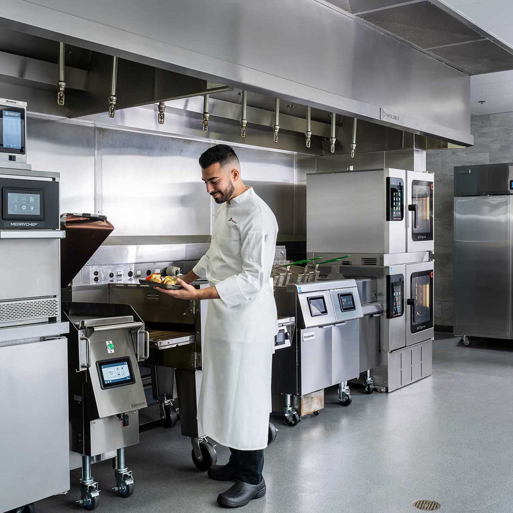 A Welbilt equipment kitchen lineup with a chef holding a plate of warm food.