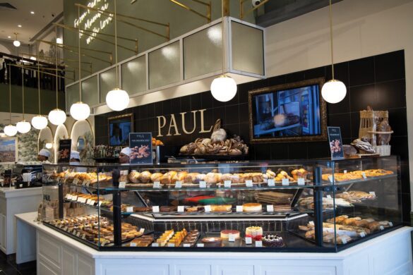 A bakery display filled with various breads, pastries, and desserts inside a modern shop with "PAUL" written on the wall behind the counter.