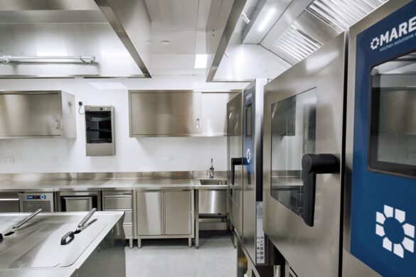 A modern commercial kitchen with stainless steel appliances, counters, and cabinets, featuring clean surfaces and industrial ovens.