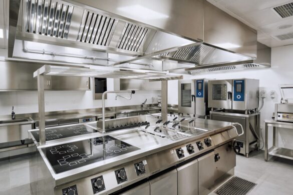 A modern commercial kitchen with stainless steel appliances, induction cooktops, ovens, ventilation hoods, and clean, organized surfaces.