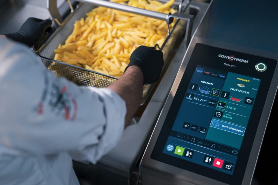 A person in a chef's uniform uses a touchscreen fryer to cook a basket of French fries, with various cooking options shown on the display.