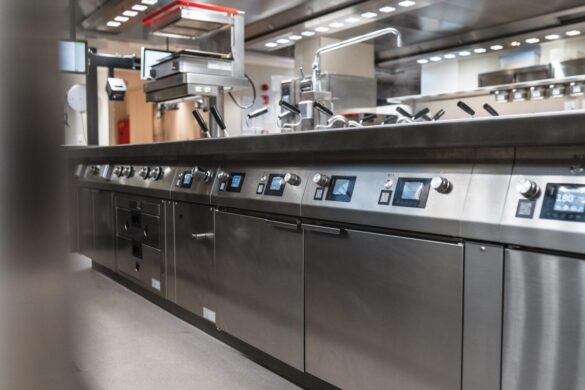 A modern commercial kitchen with stainless steel appliances, digital controls, and various cooking equipment arranged along a long countertop.