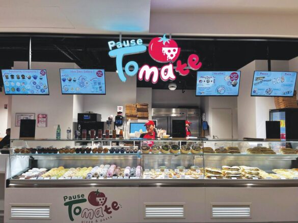 A food counter labeled "Pause Tomate" displays various pastries and dishes, with a staff member behind the counter and menu boards overhead.