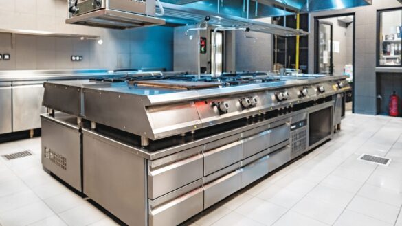 A modern commercial kitchen with stainless steel appliances and countertops, featuring multiple gas stoves, ovens, and overhead vents.